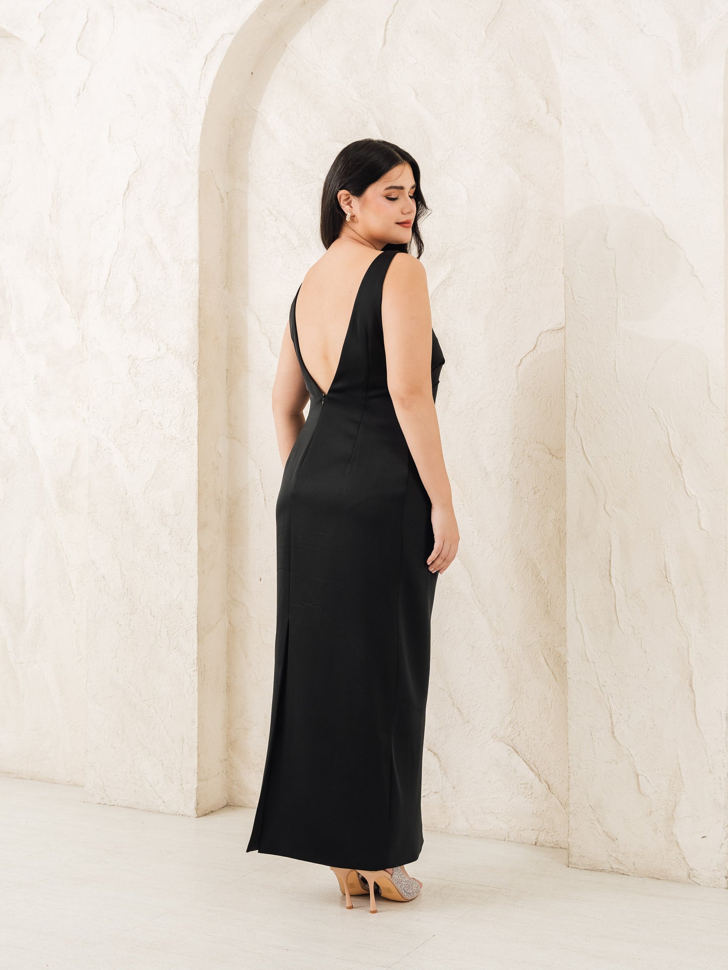 Fleur Elize black column dress with deep V-back, rear view against arched studio wall